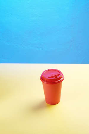 A red coffee plastic mug stands on a yellow table with blue empty space for mock upの写真素材