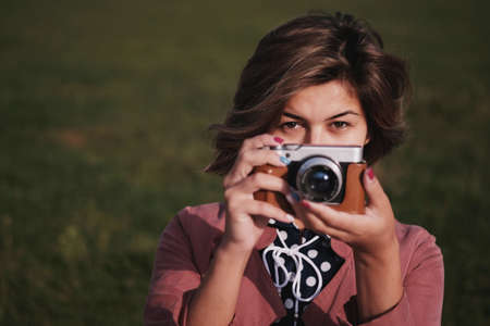 A girl on a green darc background with a mirrorless camera in her hands and looks to the frame with empty spaceの写真素材