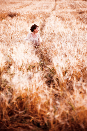The european girl goes or seat on the golden field of rye and looks away with a free copy spaceの写真素材