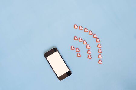 Mock up of a mobile phone come out from it red cut out paper hearts on a blue background in the form...