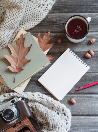 Autumn background on a wooden table with a knitted wool shawl, an old camera, autumn oak leaves and acorns, tea in a metal mug and a notepad with a pencil. Cozy warm mockupの写真素材