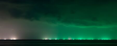 Night sky over ocean in Phu Quoc Island illuminated by green and white lights of fishermen boats