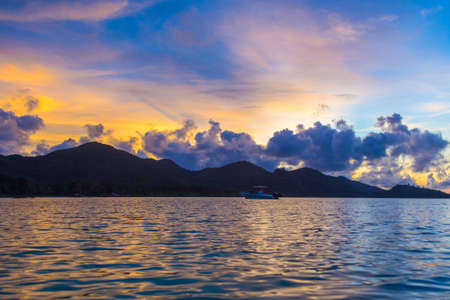 Sea, boat and mountain at sunset on Praslin island, Seychelles.の写真素材