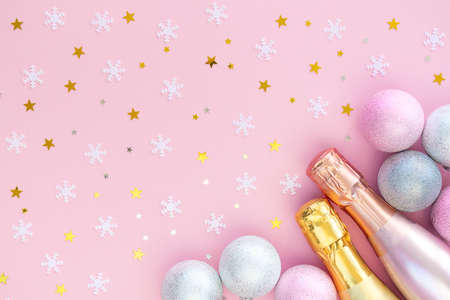 Two beautiful bottles of champagne, silver Christmas balls, snowflakes and gold stars on a pink...