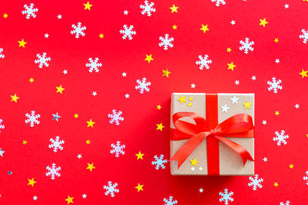 Christmas gift decorated with a red ribbon bow. Against the background of snowflakes, gold and...