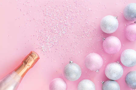 A bottle of champagne on a pink background with silver Christmas balls and sparkles. Beautiful...