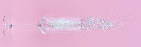 Banner with a glass of wine and scattered glittering sparkles on a pink background.の写真素材