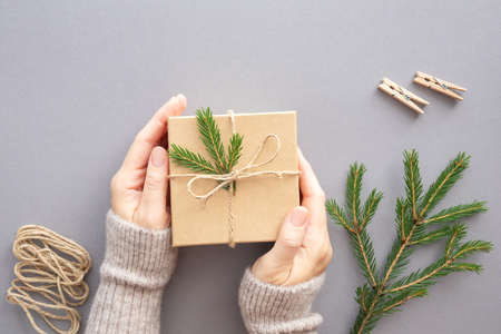 Female hands decorate a Christmas gift box, rope and fir branch on a gray background. Ecological concept, natural decorations. Flat lay, copy space.の写真素材