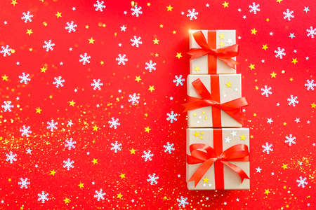 Three beautiful gifts are decorated with a ribbon. On a red background with gold and silver stars and snowflakes. Postcard for Christmas and New Year.の写真素材