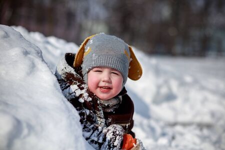 Portrait of a beautiful little child in the snow. Large snowdrifts of snow. Gray hat with ears and a...