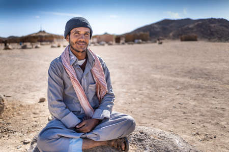 Sahara desert, Egypt - December 22, 2019: Bedouin portrait in the desert on a background of sand. Bedouin in a bathrobe and hat.のeditorial素材