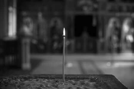 A lonely candle burns in a church. Orthodox Greek Church in Jerusalem. Black and white photo. Blurred background.の写真素材