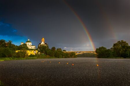 A rare event. Double rainbow in the blue sky over the city. Landscape on the river during the rain....