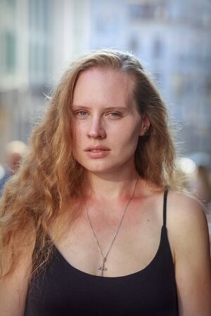 Portrait of a beautiful woman with long flowing hair and blue eyes. A woman is wearing a black dress. The girl has a pectoral cross.の写真素材