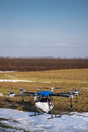 A beautiful blue agrodron stands on the field. Wheat grows. The snow has not melted yet. Agrodrons are ready to spray fertilizer.の写真素材