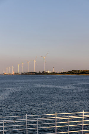 Beautiful windmills in the port of Rotterdam. Beautiful sunset on the sea coast. The Blue North Sea and Water surface. The lighthouse and shore are lit by the sunset sun.の写真素材