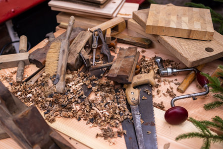 Cluttered woodworking bench with hand saw, brace drill, chisels, and wood shavings, showcasing traditional craftsmanship and active carpentry.の写真素材