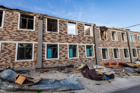 Bila Tserkva, Kyiv region, Ukraine - 09.06.2025: Two story brick building with patterned facade shows partial roof collapse, broken windows, and scattered debris damage suggests recent event.の写真素材