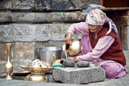 Naggar, INDIA - JULY 17: An old Indian woman cleans the dishes out of the temple. Special dishes which make offerings to God in the temple. July 17, 2013 in Naggar, Kullu Valley, Himachal Pradesh, India.のeditorial素材
