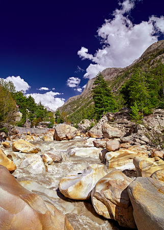 The Ganges River flows across the town. Houses in rocky river valley and green forest against snow capped mountain in the distant. Panoramic view of river. Gangotri. Uttarakhand. India.の写真素材