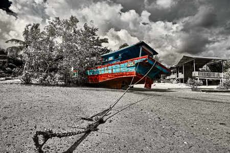 The sea tide with a old colorful asian fishing boats and dramatic sky on the background. Traditional asian fishing village, Langkawi island, Malaysia. Color in bw, color splash effect.の写真素材