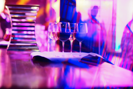 Glasses with red and white wine in colorful lights at the party. Picture with beautiful bokeh.