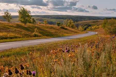 Road running through hills early morning light. Autumn rural landscape with a fields, and highway.の写真素材