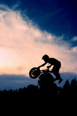 The silhouette of a motorcyclist at sunset. Moto rider making a stunt on his motorbike.の写真素材