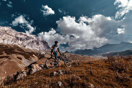 Elbrus, Kabardino-Balkaria, Russia - Sep 2021: Mountain biking in Elbrus. Cyclist on the top of a hill and enjoying view of the mountains. MTB bicycle rider standing at cliff.のeditorial素材