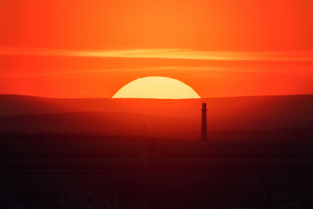 Telephoto lens panoramic shot of cityscape view megalopolis during sunset with giant sun at summer eveningの写真素材