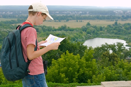 Boy with binoculars and backpack looks at the map on a hike の写真素材