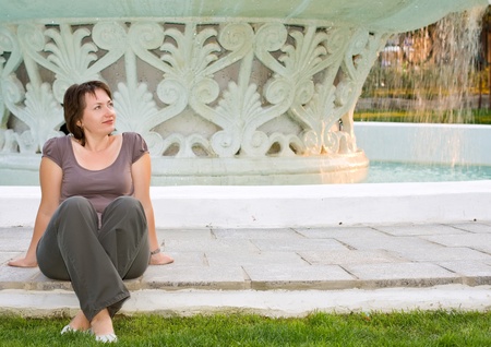 young beautiful woman relaxes in front of fountain at sunset の写真素材