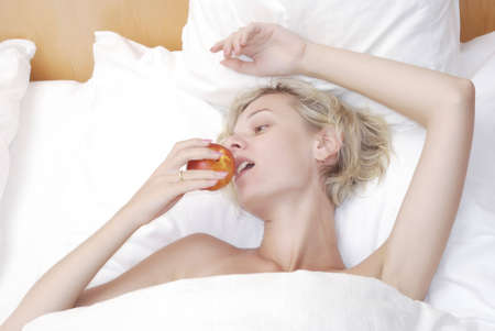 Beautiful young woman eating fruits in bedの写真素材