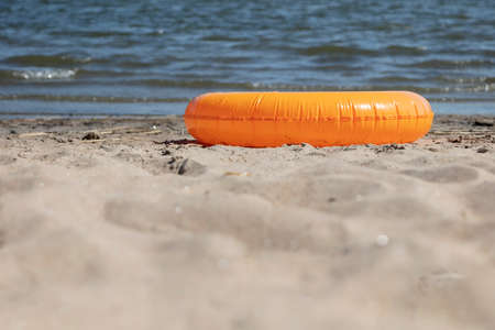 Orange rubber ring for swimming on the sandy shore at the edge. Summer sunny day by the sea. High...