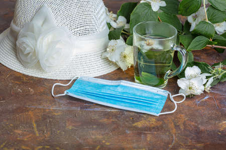 Summer hat, medical mask, jasmine tea in a mug, flowers. Still life. High quality photoの写真素材
