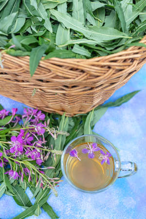 Traditional Russian herbal drink Ivan tea in a transparent cup. Close-up, leaves of Ivan tea, fireweed, wicker basket background. High quality photoの写真素材