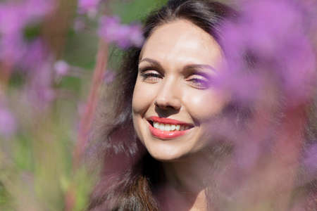 Portrait of a woman, close-up, brunette with green eyes, in purple colors, ivan tea, sunny day. High quality photoの写真素材