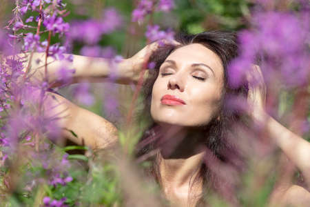 Portrait of a woman, close-up, brunette with green eyes, in purple colors, ivan tea, sunny day. High quality photoの写真素材