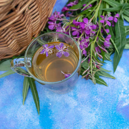 Traditional Russian herbal drink Ivan tea in a transparent cup. Close-up, leaves of Ivan tea, fireweed, wicker basket background. High quality photoの写真素材