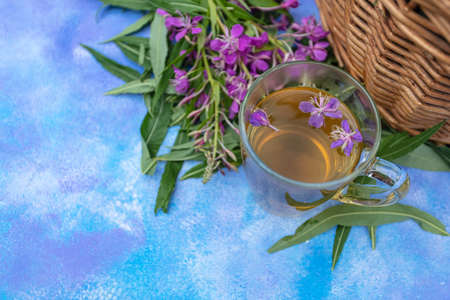 Traditional Russian herbal drink Ivan tea in a transparent cup. Close-up, leaves of Ivan tea, fireweed, wicker basket background. High quality photoの写真素材