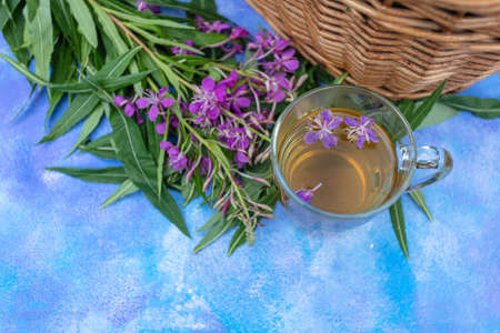 Traditional Russian herbal drink Ivan tea in a transparent cup. Close-up, leaves of Ivan tea, fireweed, wicker basket background. High quality photoの写真素材