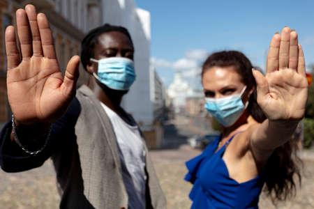 Portrait of a young European woman and African man wearing a mask in a city street.