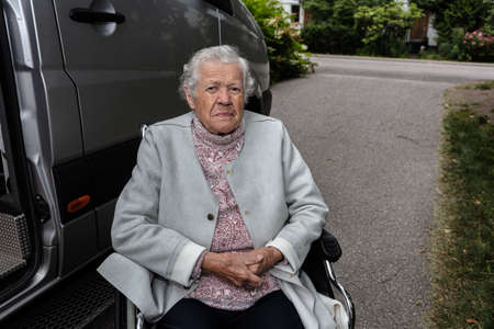 An elderly woman in a wheelchair for the disabled by a car for people with disabilities. the concept...