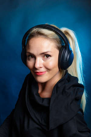 Blonde woman with headphones. smiling, looking at the camera. Photography in the studio, dark...