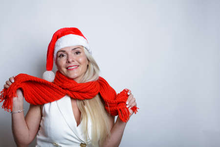 Beautiful blonde, in a white suit with a red scarf and a Santa hat, posing in front of the camera, studio light background, Happy New Year concept. High quality photoの写真素材