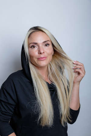 Portrait of a beautiful blonde, athletic woman, in a black jacket with a cap, standing on a white background. She poses for the camera. High quality photoの写真素材