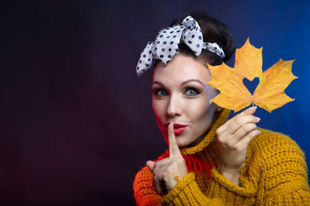 A woman brings a maple leaf with a cut out heart to her face and holds a finger to her lips Photo in...