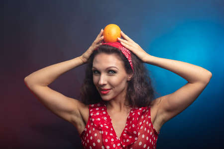 Brunette with an orange. Studio, dark background She holds a fruit on her head. High quality photoの写真素材