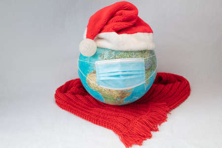 The globe is wearing a medical mask Christmas cap and red warm scarf. White background. concept, our world is infected with coronavirus. Christmas, new year stay home quarantined. High quality photoの写真素材