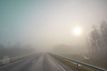 The sun is in the fog. Road and forest. Poor visibility. Autumn morning in November. Photo through the windshield of a car. High quality photoの写真素材